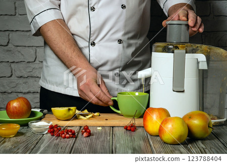 Hands skillfully operate a juicer in a rustic kitchen surrounded by fresh fruits such as apples and viburnum. The process reflects essence of healthy living and culinary creativity. Making fruit juice 123788404