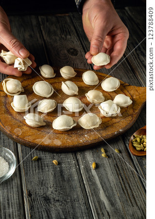 Hands are skillfully shaping dumplings on a wooden board, surrounded by flour and spices in a warm kitchen. The afternoon light enhances the inviting atmosphere of the cooking space Hands are skillfully shaping dumplings on a wooden board, surrounded by flour and spices in a warm kitchen. The afternoon light enhances the inviting atmosphere of the cooking space 123788409