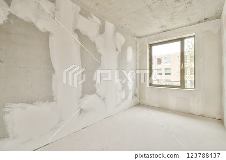 A newly constructed room featuring bare, unfinished walls and a single window allowing natural light to enter, creating a minimalist atmosphere. 123788437