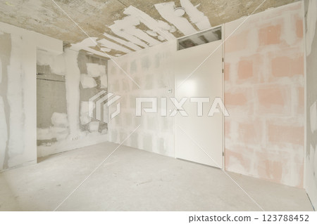 An empty room showcasing a modern architectural style with unfinished walls and a distinct door. The space highlights raw textures and minimal design elements. An empty room showcasing a modern architectural style with unfinished walls and a distinct door. The space highlights raw textures and minimal design elements. 123788452