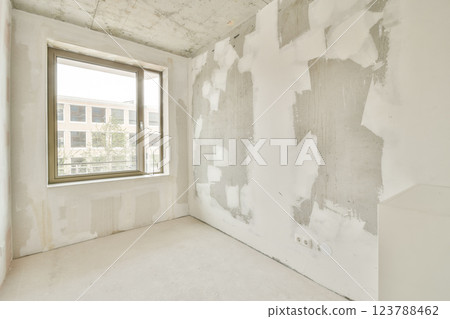 A vacant room with plastered walls and a large window revealing an outdoor view. The space is in the midst of renovation, showcasing unfinished surfaces. A vacant room with plastered walls and a large window revealing an outdoor view. The space is in the midst of renovation, showcasing unfinished surfaces. 123788462
