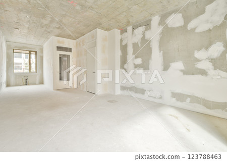 An empty room featuring unfinished walls and a smooth, bare floor, illuminated by natural light from a nearby window, creating a spacious atmosphere. 123788463