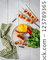 Grilled sausages and vegetable skewers with vegetables and herbs on a light background. View from above 123789365