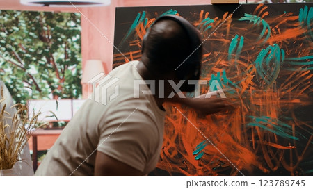 Artist listening to music and creating an abstract painting with his fingers, showing his skills and contemporary ideas in art studio. Creative process finger painting for vibrant artwork. Camera A. 123789745