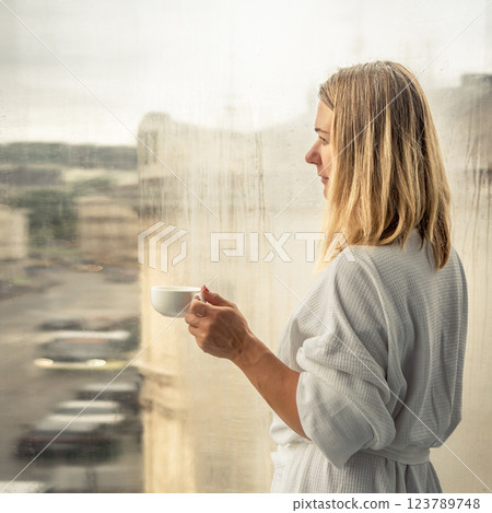 Woman in elegant robe drinking coffee in hotel room and standing near window 123789748