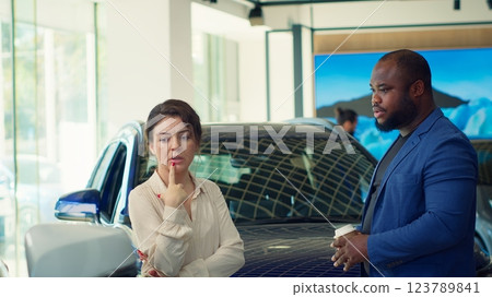Customers walking in car dealership browsing through available models, trying to and select ideal investment choice. Husband and wife in showroom looking to make vehicle purchase, camera A Customers walking in car dealership browsing through available models, trying to and select ideal investment choice. Husband and wife in showroom looking to make vehicle purchase, camera A 123789841