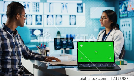 Woman general practitioner and patient looking at green screen on laptop, recommending pills and medicine during check up. Indian people discussing diagnostic report and recovery. Camera B. 123789871