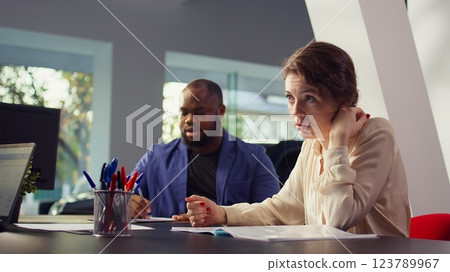 Car dealership salesman giving couple documentation to read after agreeing terms. Agent giving sale contract for clients to sign after they decide to make purchase, camera B Car dealership salesman giving couple documentation to read after agreeing terms. Agent giving sale contract for clients to sign after they decide to make purchase, camera B 123789967