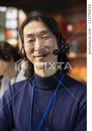 Portrait of cheerful senior call center agent dealing with unhappy customers, speaking with them using headset in office. Jolly experienced customer support representative handling clients complaints 123790018