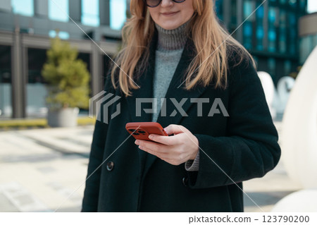 Business professional woman in winter black coat walking on old city street checks her smartphone with AI chatbot for online information in city town, Business professional woman in winter black coat walking on old city street checks her smartphone with AI chatbot for online information in city town, 123790200