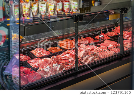 Meat counter. Butcher shop fridge counter with assortment of raw meat.. Glass display case in butcher shop filled with fresh meat products. Various cuts of beef, pork, sausages are arranged for buyers Meat counter. Butcher shop fridge counter with assortment of raw meat.. Glass display case in butcher shop filled with fresh meat products. Various cuts of beef, pork, sausages are arranged for buyers 123791160