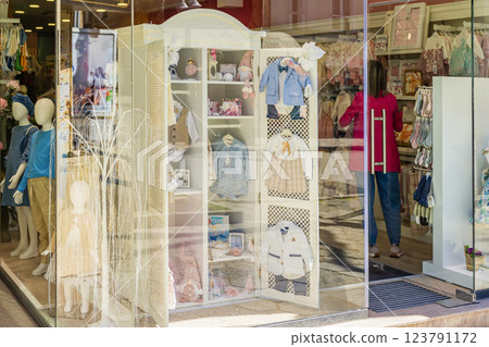 Elegant baby clothing display in boutique storefront with reflections of street. Stylish pastel outfits for infants and toddlers, cozy shopping atmosphere Elegant baby clothing display in boutique storefront with reflections of street. Stylish pastel outfits for infants and toddlers, cozy shopping atmosphere 123791172