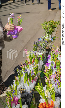 Elderly woman holding a small bouquet of hyacinths at an outdoor flower market. Fresh spring flowers wrapped in delicate pink and purple paper, spring mood 123791173