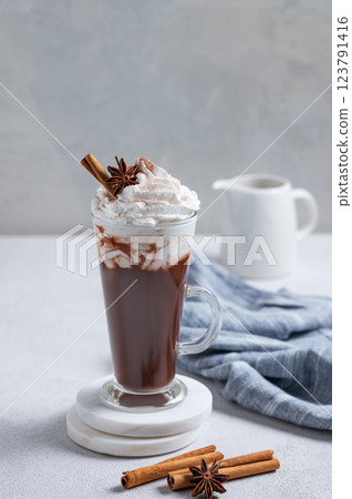 Hot chocolate with whipped cream, cinnamon and spices in a tall glass on a light background 123791416