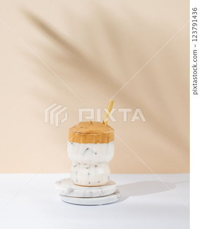 Korean whipped drink Dalgona coffee in a glass on a white beige background with morning shadow. Korean whipped drink Dalgona coffee in a glass on a white beige background with morning shadow. 123791436
