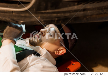 Focused Auto Mechanic Inspecting Vehicle Underneath Using Safety Equipment in Garage Workshop 123791648