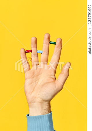 Male hand holding various pills balanced on fingers over yellow background 123791662