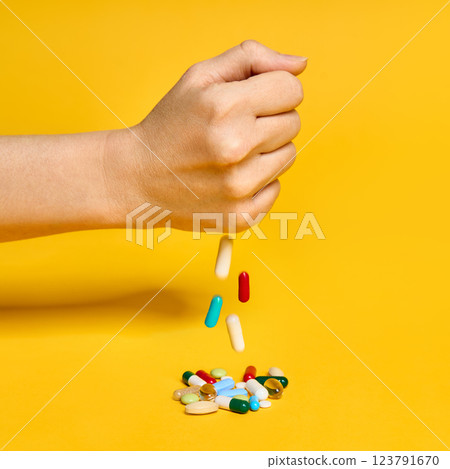 Female hand throws various pills over yellow background 123791670