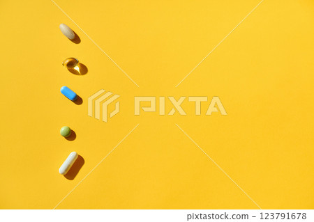 Various pills and vitamins of different colors and shapes at yellow background 123791678
