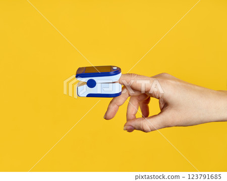 Pulse Oximeter digital device on finger measuring oxygen saturation over yellow background. 123791685