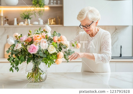 Elderly woman arranging a bouquet of fresh flowers in a modern kitchen while enjoying a peaceful afternoon 123791928
