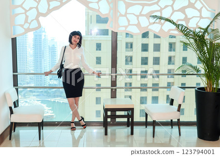 A woman in a business suit is waiting for an elevator in a multi-story building, standing at a panoramic window A woman in a business suit is waiting for an elevator in a multi-story building, standing at a panoramic window 123794001
