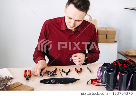 Male jewelry artisan meticulously crafting handmade accessories in a modern workspace. Handmade business, artisan craftsmanship, independent maker Male jewelry artisan meticulously crafting handmade accessories in a modern workspace. Handmade business, artisan craftsmanship, independent maker 123794370
