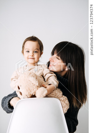 Mother and child bonding with a toy bear, family love, early childhood, tender moments, cozy indoor portrait, maternal affection, parenthood. 123794374