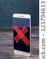 Phone stands upright on table with its screen covered by red X tape 123794613