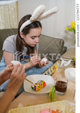 A young girl wearing bunny ears paints a white Easter egg with a brush. A young girl wearing bunny ears paints a white Easter egg with a brush. 123794777