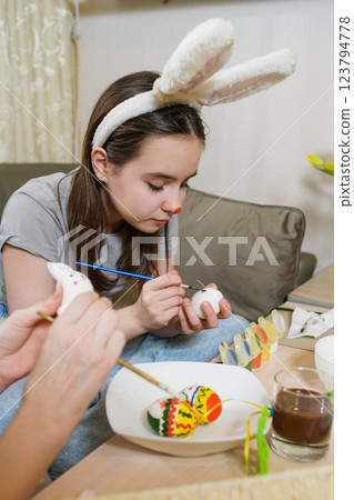 A young girl wearing bunny ears paints a white Easter egg with a brush. A young girl wearing bunny ears paints a white Easter egg with a brush. 123794778