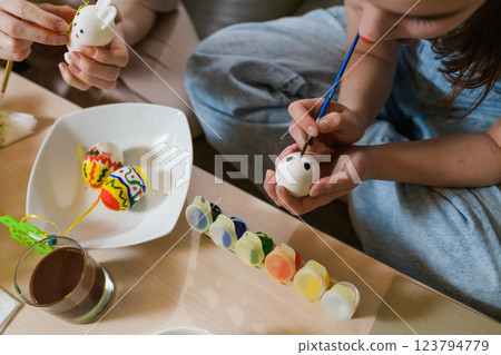 A girl paints black eyes on a white Easter egg while holding it carefully. A girl paints black eyes on a white Easter egg while holding it carefully. 123794779