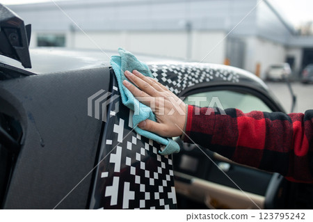 A professional car cleaner meticulously washing a shiny vehicle using a pressure hose and foam. The man focuses on the car's exterior, ensuring a spotless, polished finish at an auto detailing station 123795242