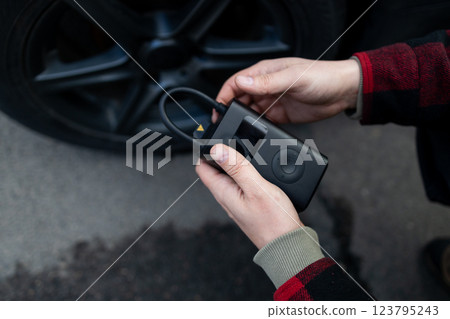 Close up of man hand holds a wireless portable air pump for inflating car tires. Self service, maintenance and safety.  123795243