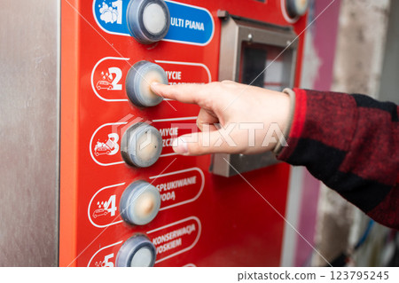 Self service car wash station featuring a red and white theme, a control panel, blue hose, instructional icons, and trees in the background under daylight. Self service car wash station featuring a red and white theme, a control panel, blue hose, instructional icons, and trees in the background under daylight. 123795245