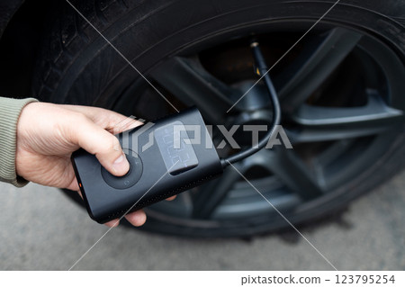 Close up of man hand holds a wireless portable air pump for inflating car tires. Self service, maintenance and safety.  123795254