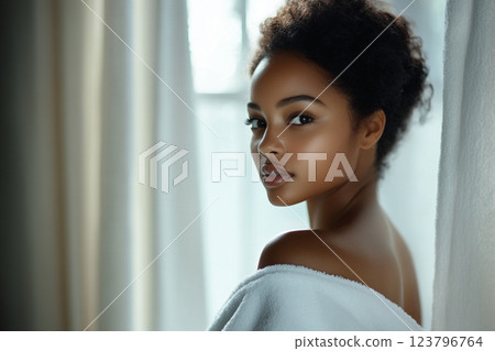 serene portrait of young woman with natural curls, wrapped in towel, showcasing her radiant skin and gentle expression. soft lighting enhances calm atmosphere 123796764