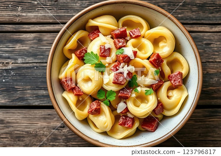 Homemade Mediterranean Tortellini with Artisanal Cured Meats, Aged Parmesan, and Fresh Herbs on Rustic Wooden Table Setting 123796817