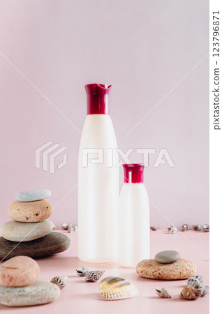 Pair of bottles with cosmetic products among stones and shells on pink vertical view Pair of bottles with cosmetic products among stones and shells on pink vertical view 123796871