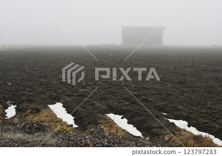 a fog-covered rural landscape with a freshly plowed field stretching toward the misty horizon 123797283