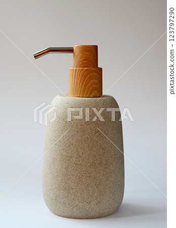 A beautifully designed soap dispenser featuring a textured stone body with a wooden pump and stainless steel spout 123797290
