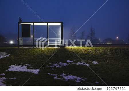 A minimalist bus stop illuminated by glowing panels on a foggy evening 123797531
