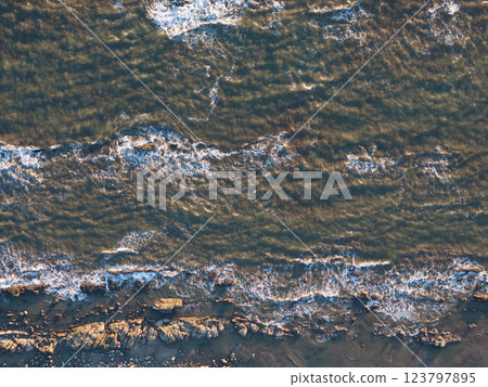 Waves crashing on rocky shore in golden hour sunlight with gentle ripples 123797895