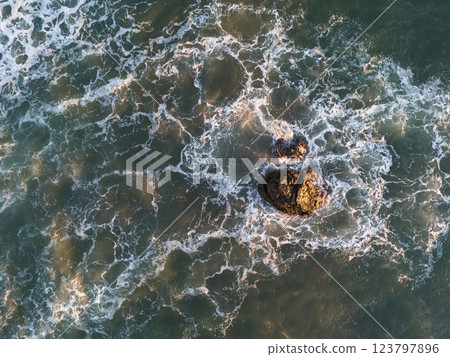 Waves crashing around rocky outcrop in ocean at sunset 123797896