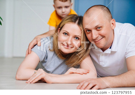 A man and a woman with a son are sitting on the floor in a bright room  123797955