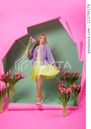A beautiful elderly woman with a bouquet of tulips comes out of a torn pink background. A beautiful elderly woman with a bouquet of tulips comes out of a torn pink background. 123798179