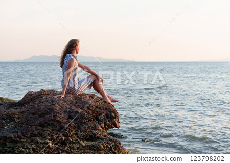 Woman relaxing on rock contemplating inspiring ocean view at sunset 123798202