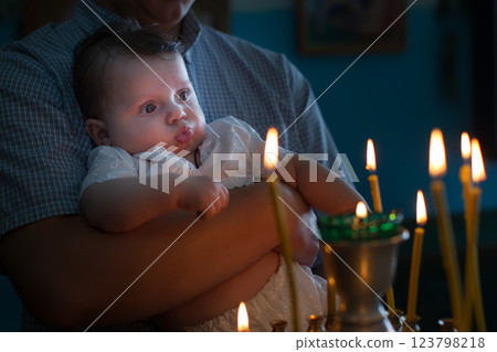 The father's hands hold the baby in his arms in the church. The kid looks at the candles burning in the temple. Child in church 123798218
