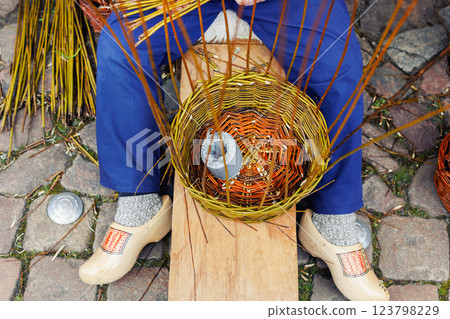Artisan Dutch person weave natural wicker strips handmade basket sitting street traditional fair Holland festival street. Man make rustic vintage Netherlands craft items. Basketry handicraft workshop 123798229