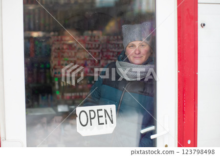 A woman looks through the glass door of a store marked "open." 123798498